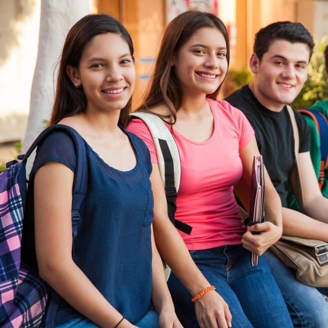 Grupo de estudiantes adolescentes sonriendo con mochilas en la escuela, ideal para promocionar clases de idiomas con descuento y promociones educativas
